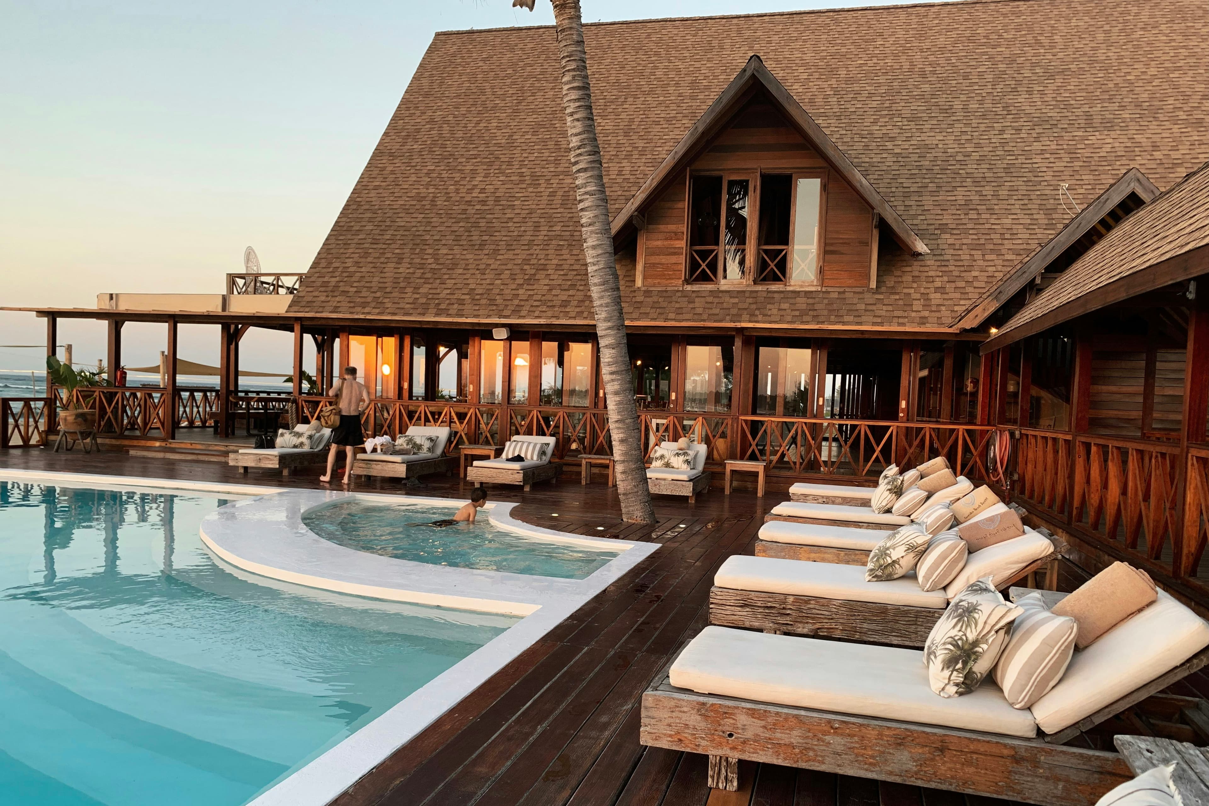 A resort pool below a thatched lodge at sunset